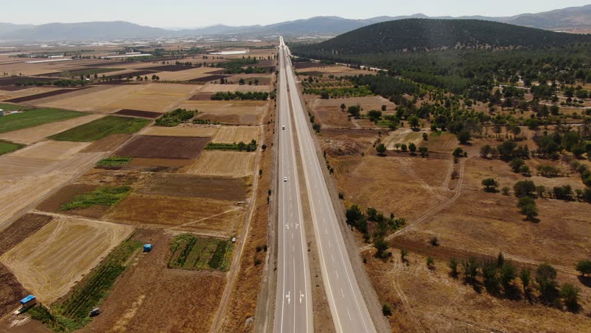A flat highway in a rural landscape. Aerial view of the natural-geometric contrast between agricultural fields and forested hills. Turkey.