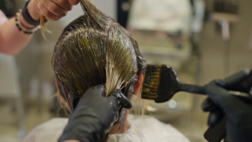 Close-up of a hairdresser applying treatment to a girl's hair. Hair health care in a beauty salon.