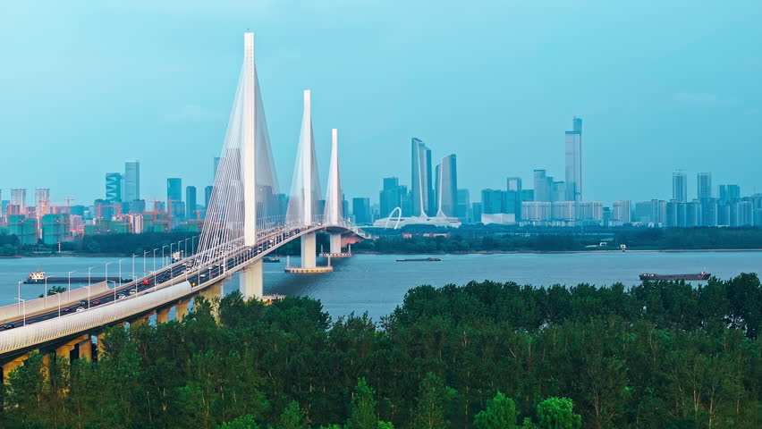Aerial shot of a modern cable-stayed bridge spanning a wide river with the city skyline in Nanjing, China.