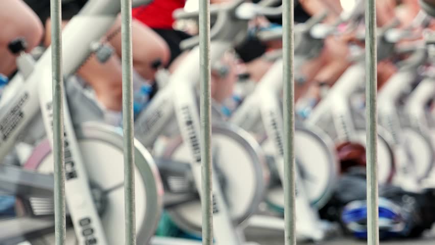 Athletes pedaling on exercise bikes during sports day behind a fence