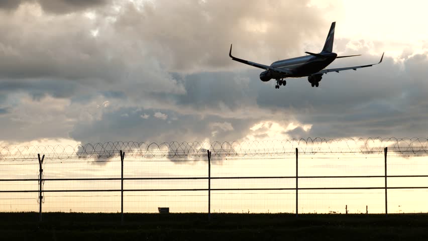 Passenger plane landing at airport behind barbed wire fence at sunset