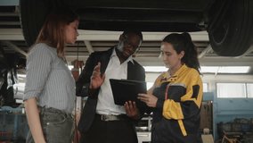 Latin mechanic manager explains to White female client and Black insured agent about EV car undercarriage fix work, claim warranty service maintenance at automotive garage, transportation industry. - Powered by Shutterstock - Get 15% off with code: PIKWIZARD15