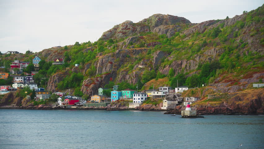Floating over quaint little town on edge of ocean backing onto large cliff on a cloudy autumn day. St Johns Newfoundland, Canada