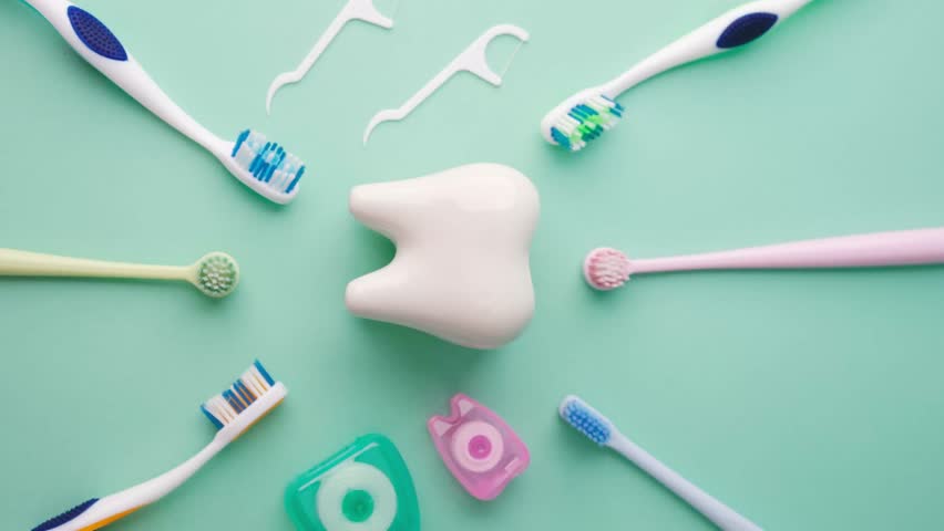 Tooth shape object with toothbrushes and dental floss picks on teal background