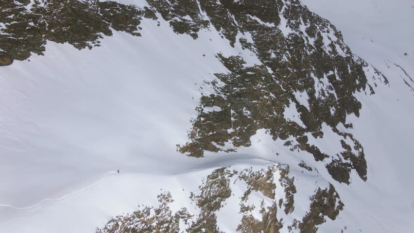 Drone following a man skiing down snowy mountain slopes, sunny, winter day