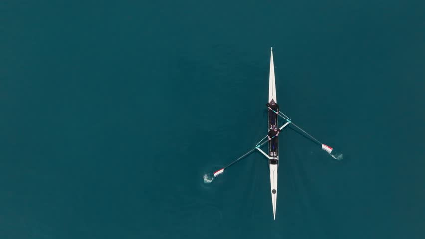 Two athletes rowing a sculling boat on calm blue water, teamwork and endurance in competitive sport. Rowers are practicing sport rowing. Rowers in a racing boat row in slow motion video 120fps.