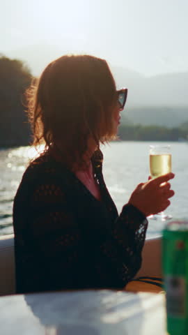 Rich woman drinking cool champagne alone on her own yacht in summer weekend. Yacht trip by sea or ocean, lady admiring picturesque mountains on coastline, luxury life and wealth, lazy day on yacht