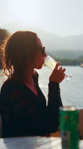 Rich woman drinking cool champagne alone on her own yacht in summer weekend. Yacht trip by sea or ocean, lady admiring picturesque mountains on coastline, luxury life and wealth, lazy day on yacht