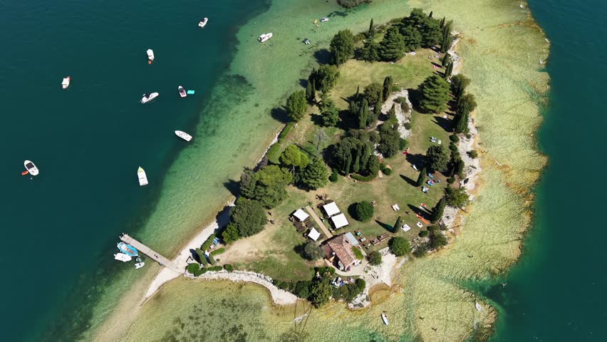 Aerial view in 4K drone video of Isola di San Biagio, Lake Garda, Italy, surrounded by turquoise waters.