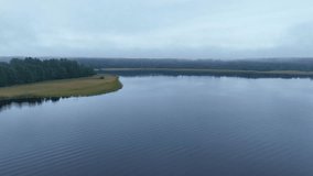 Drone shot above a misty lake with gentle waves, grassy shoreline, trees, and haze surrounding the water. - Powered by Shutterstock - Get 15% off with code: PIKWIZARD15
