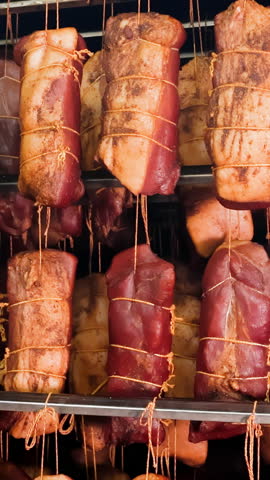 Assorted Meats Curing in a Smokehouse, Diverse cuts of meat being cured, tied up with strings in a smoking chamber.