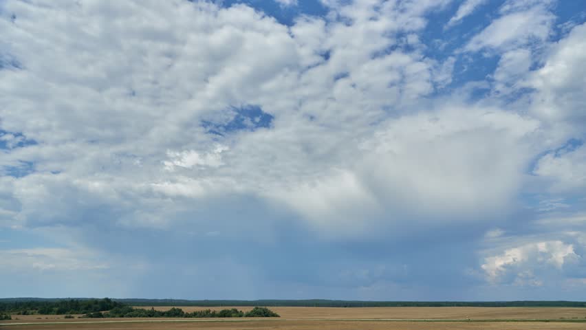 A timelapse of clouds over an agricultural field. A spring landscape with a forest, an empty field and clouds. A harvested wheat field
