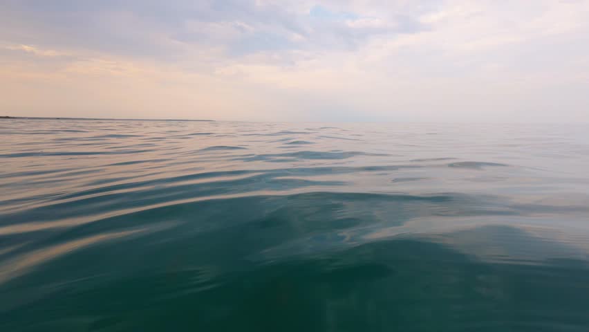 Slow motion video of calm evening sea with gentle ripples and soft pastel reflections. Tranquil ocean surface under a serene sky, creating a peaceful and meditative mood