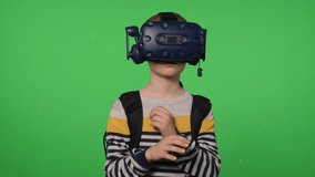 Portrait of a young boy wearing virtual reality glasses, on a green backdrop. He is watching a video, moving his hand through the air, flipping through virtual pages. VR headset. Chroma key. - Powered by Shutterstock - Get 15% off with code: PIKWIZARD15