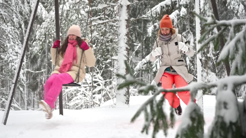 Middle-aged mother and teenage daughter enjoy winter holidays in Finland, swinging together in snowy park. Warm clothes, joyful emotions, family values, seasonal lifestyle and vacation mood.