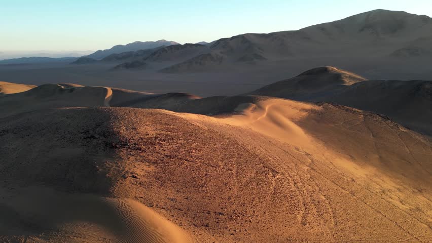 Aerial drone view of sweeping sand dunes in the southern Atacama Desert, glowing in warm evening light.