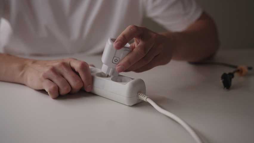 Close-up of unrecognizable man plugging smart plug into white extension cord on table. Concept of smart home technology and energy management. Shooting in slow motion.