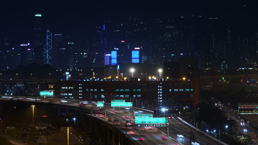 Illuminated Skyscrapers Rising Against The Night Sky, Showcasing The Vibrant Hong Kong Skyline. Traffic Flows Along The Highway, Creating Dynamic Light Trails In This Bustling Metropolis