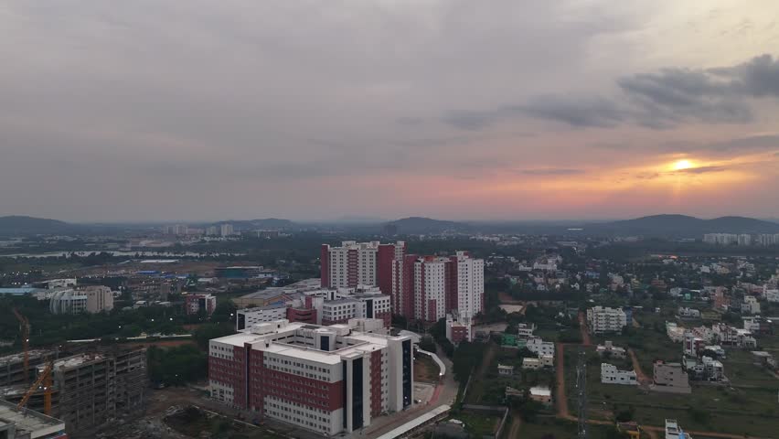 An aerial video of a mixed urban landscape. The scene includes completed modern buildings, an ongoing construction site, and a natural lake, illustrating the rapid growth of a city. VIT Chennai
