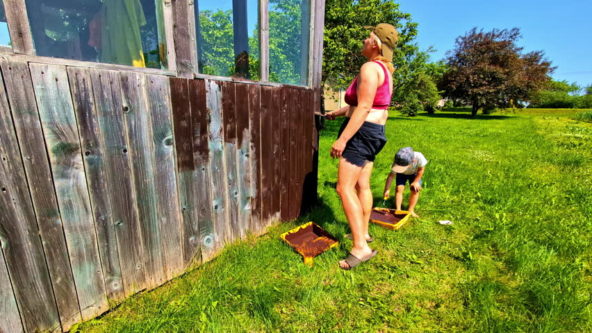 Woman painting weathered wooden wall with children helping in backyard