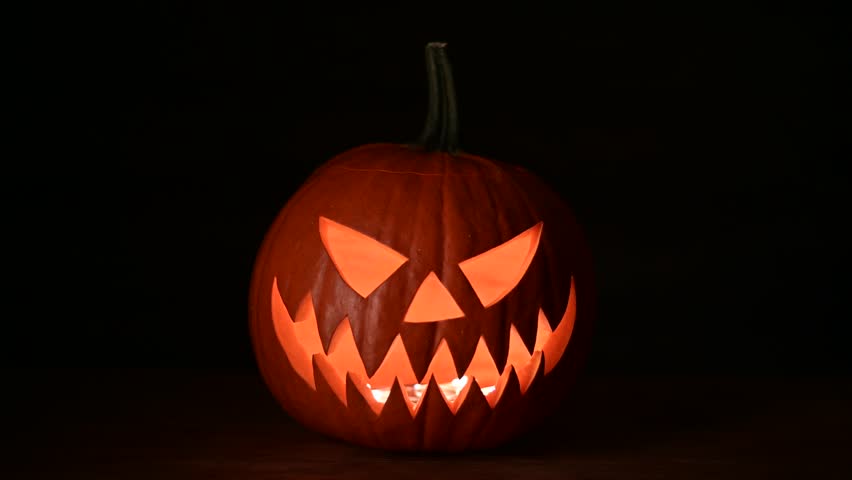 Glowing jack-o'-lantern lit from inside on wooden table on black background. Halloween concept. UHD 4k video