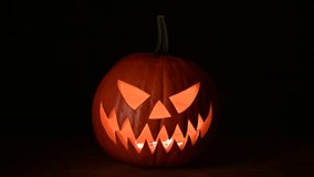 Glowing jack-o'-lantern lit from inside on wooden table on black background. Halloween concept. UHD 4k video - Powered by Shutterstock - Get 15% off with code: PIKWIZARD15