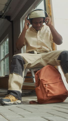 Vertical of Black mechanic resting in garage with headphones, sipping coffee and relaxing between detailing jobs