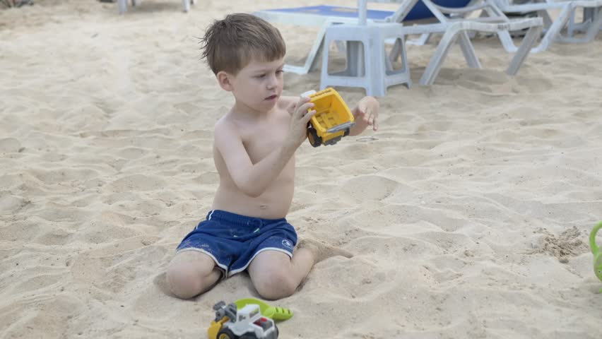 Cute child enjoying playtime on sandy beach with plastic car. Holiday vacation moment of happy childhood. Family tourism and leisure activity on summer seaside. Young boy playing with toy truck.