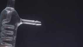 White smoke emerges from a laboratory glassware while blue liquid flows through a coil. Laboratory research concept. - Powered by Shutterstock - Get 15% off with code: PIKWIZARD15