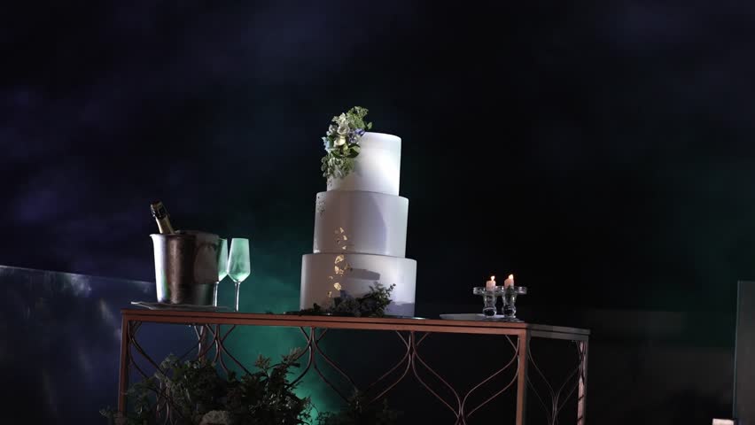 Elegant three tier wedding cake with floral decor beside champagne and glowing candles