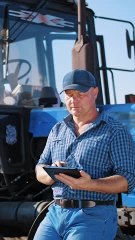 Farmer is using digital tablet. on farm field, near tractor, on farm machinery backdrop. smart farming. farming technologies