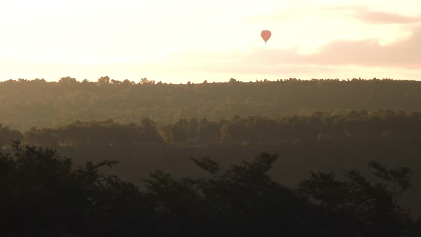 Hot air balloon drifts across the horizon during sunrise in the English countryside.