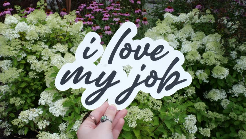 Young Woman Holds Up message of I Love My Job Wording in front of Colorful Flowers in a garden in Summer 4K Video Stock Footage