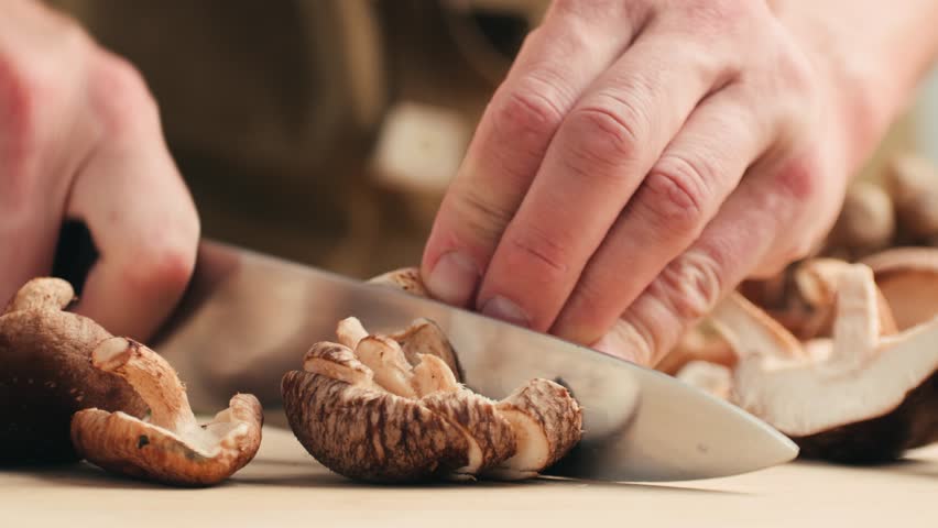 Fresh Royal oyster mushrooms, chef cooking on a wooden cutting board with knife in cafe asian restaurant kitchen, vibrant scene of food preparation