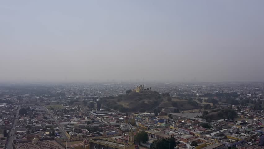 An aerial drone shot captures the iconic Santuario de Nuestra Señora de los Remedios (Church of Our Lady of Remedies) perched atop the Great Pyramid of Cholula in Puebla, Mexico.