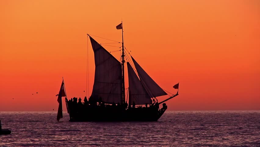 The black shadow of an old sailing ship with partying people against an orange sunset.