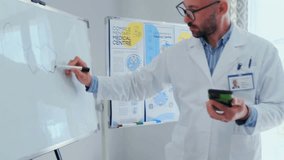 Male scientist in a white lab coat using smartphone while explaining and drawing chemical formula on whiteboard with a marker. Modern medical research, innovative technology, and scientific education. - Powered by Shutterstock - Get 15% off with code: PIKWIZARD15