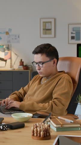 Vertical shot of Caucasian young developer sitting in leather office chair, coding and eating salted caramel peanuts
