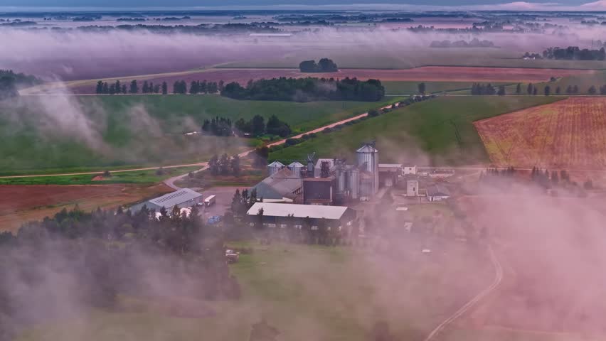 Drone view of layer of foggy clouds passing through agricultural lands during morning.