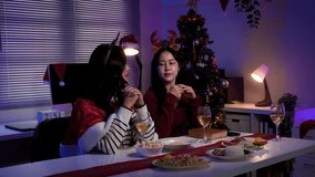 Two young Asian women bowing their heads in prayer before a Christmas meal, surrounded by friends in a festive home celebration during the holiday season - Powered by Shutterstock - Get 15% off with code: PIKWIZARD15