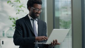 African American businessman male business man in office looking out window typing laptop smiling happy working at workplace using corporate software chatting internet browsing analyzing online data - Powered by Shutterstock - Get 15% off with code: PIKWIZARD15