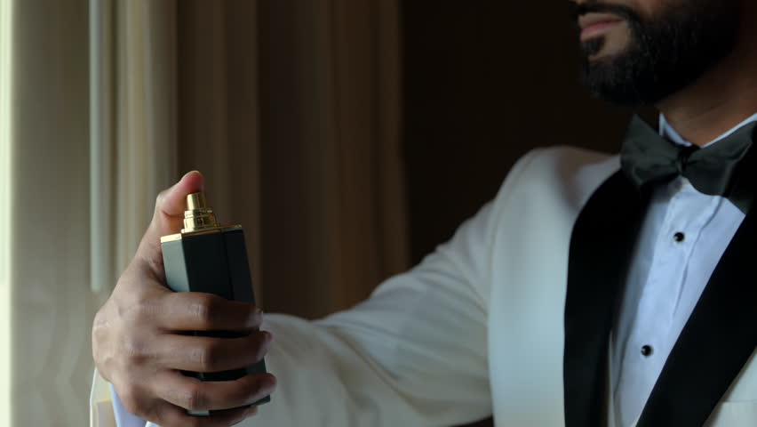 Close up view of man in white suit spraying the perfume on himself. Slow motion