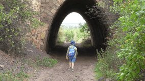 4K video of a boy with a backpack walking into a stone tunnel on a forest path. Concept of childhood adventure, exploration and journey - Powered by Shutterstock - Get 15% off with code: PIKWIZARD15
