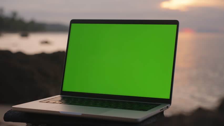Close View of Laptop with Green Screen on Rock by Ocean at Sunset, low angle, App Promotion Concept.