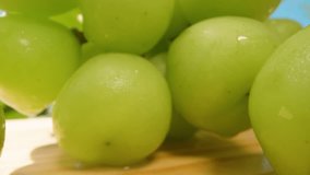 Close Up of Green Grapes with Water Droplets on Wooden Surface in Bright Outdoor Setting with Blue Sky and Green Trees, Dolly Slider, Fresh Fruit Concept. - Powered by Shutterstock - Get 15% off with code: PIKWIZARD15