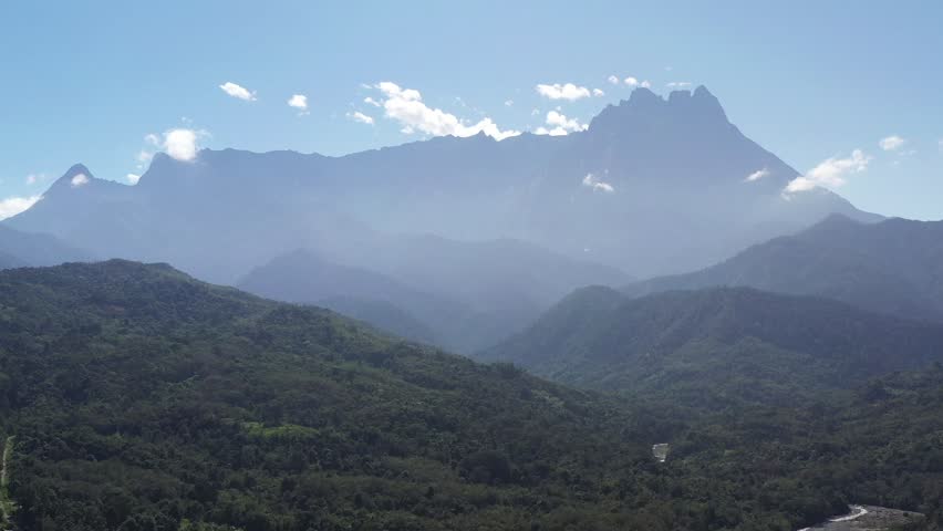 Scenic aerial view of Mount Kinabalu surrounded by lush green hills and valleys in Kota Belud, Sabah, Malaysia.