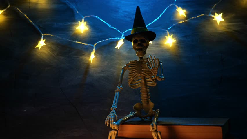 Halloween Book.Skeleton Wearing Wizard Hat on Stack of Books on chalkboard background.Spooky Stories for Halloween. 4k footage