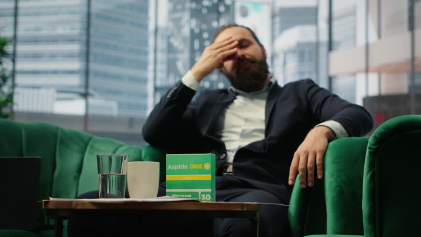 Concerned CEO taking an aspirin to ease the headache due to stress, feeling a discomfort and using painkillers. Tired uncomfortable boss deals with a migraine, burnout and tension. Camera A.