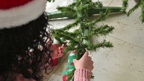 Unrecognizable woman wearing a Santa hat and a striped pink sweater sits on the floor beside a Christmas tree, knitting. - Powered by Shutterstock - Get 15% off with code: PIKWIZARD15