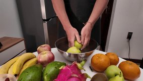 A man in an apron stands in front of a table with fruit, washing green apples in a metal bowl - Powered by Shutterstock - Get 15% off with code: PIKWIZARD15